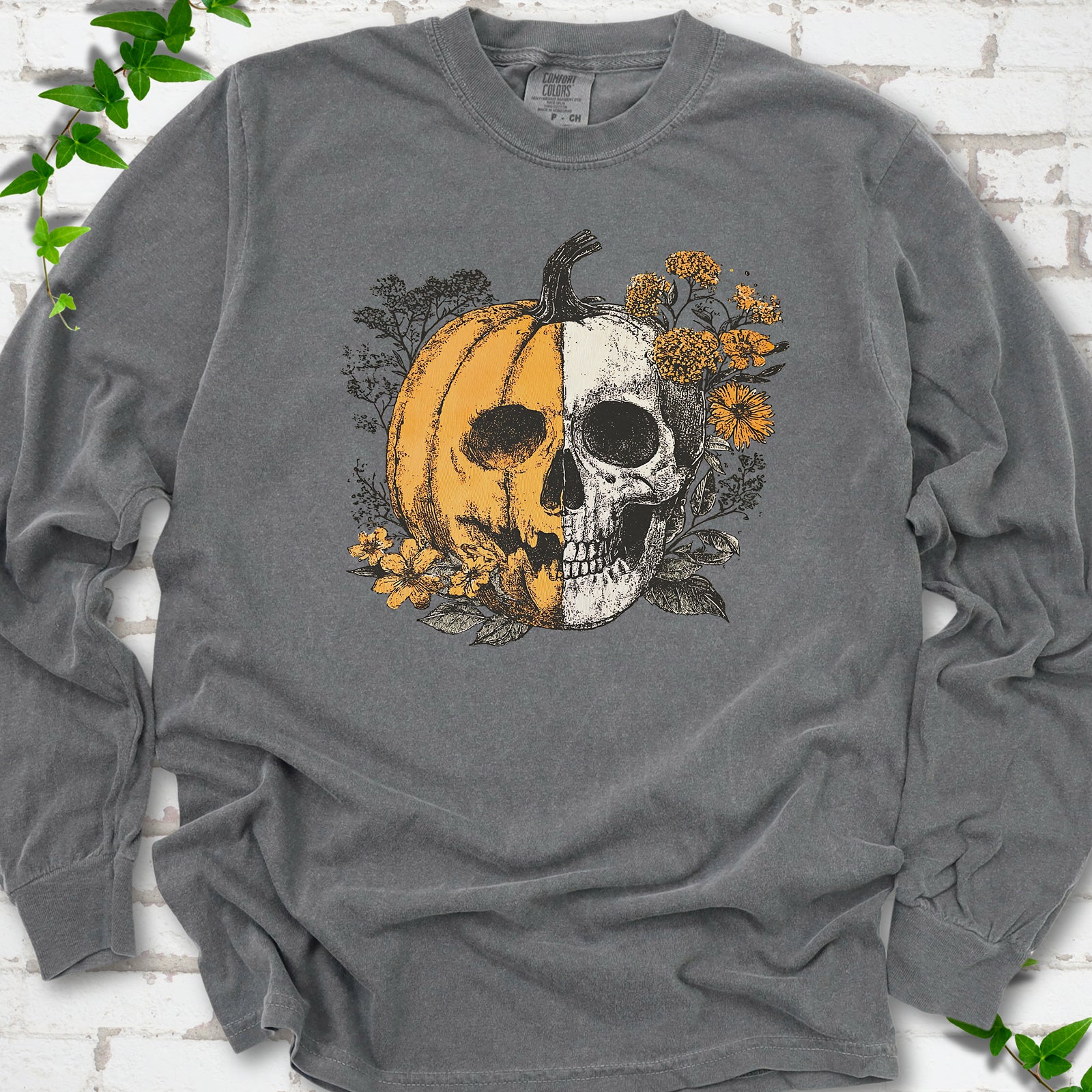 Pepper Comfort Colors® long sleeve T-shirt flat lay featuring a half-pumpkin, half-skull botanical Halloween graphic.