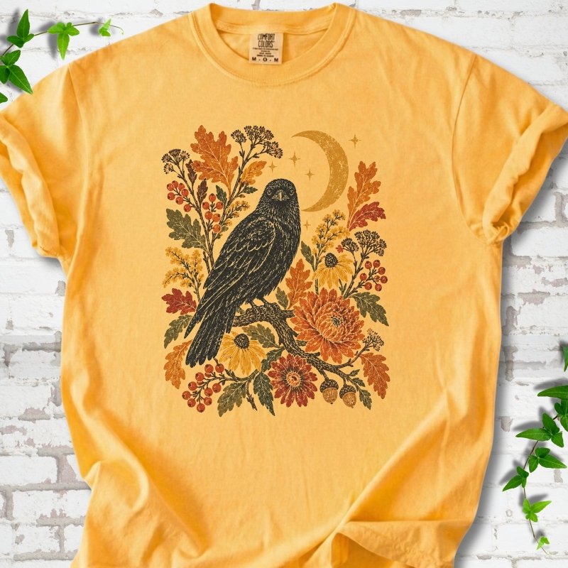 Citrus T-shirt flat lay with a black raven, crescent moon and warm autumn flowers and foliage.