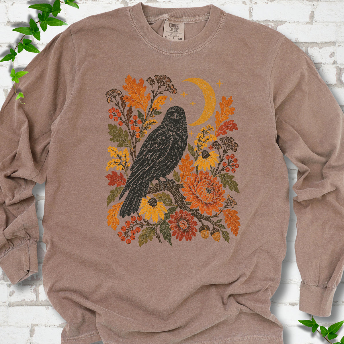 Espresso long sleeve T-shirt flat lay with a black raven, crescent moon and warm autumn flowers and foliage.