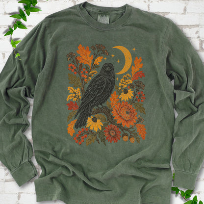 Hemp long sleeve T-shirt flat lay with a black raven, crescent moon and warm autumn flowers and foliage.