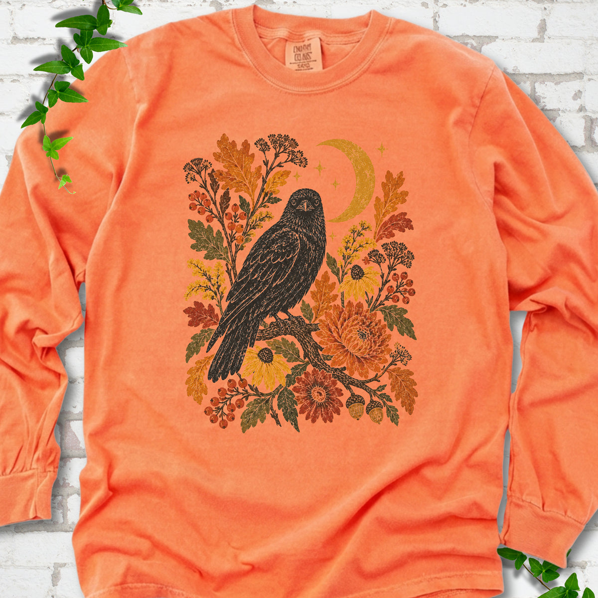 Melon long sleeve T-shirt flat lay with a black raven, crescent moon and warm autumn flowers and foliage.