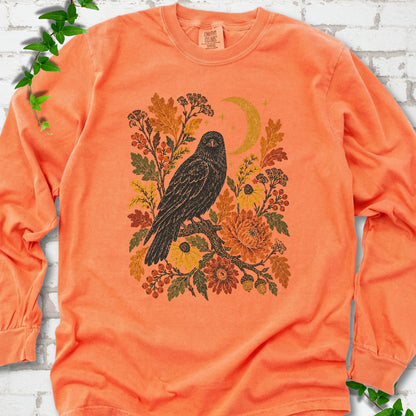 Melon long sleeve T-shirt flat lay with a black raven, crescent moon and warm autumn flowers and foliage.