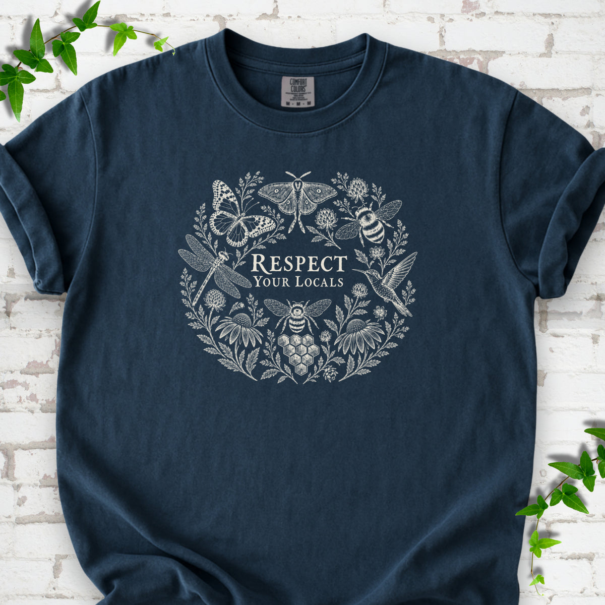 Midnight Comfort Colors® T-shirt flat lay featuring the words “Respect Your Locals” surrounded by pollinating insects, a hummingbird and flowers.