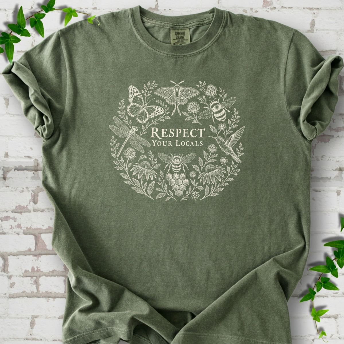Moss Comfort Colors® T-shirt flat lay featuring the words “Respect Your Locals” surrounded by pollinating insects, a hummingbird and flowers.