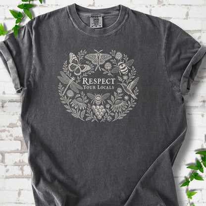 Pepper Comfort Colors® T-shirt flat lay featuring the words “Respect Your Locals” surrounded by pollinating insects, a hummingbird and flowers.