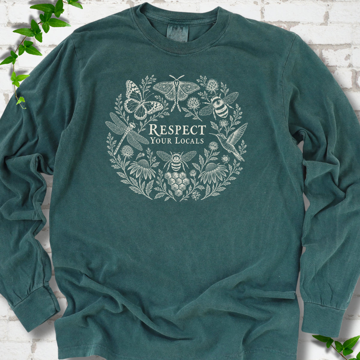 Blue Spruce Comfort Colors® long sleeve tee flat lay featuring the words “Respect Your Locals” surrounded by pollinating insects, a hummingbird and flowers.