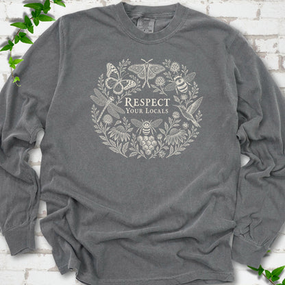 Pepper Comfort Colors® long sleeve tee flat lay featuring the words “Respect Your Locals” surrounded by pollinating insects, a hummingbird and flowers.