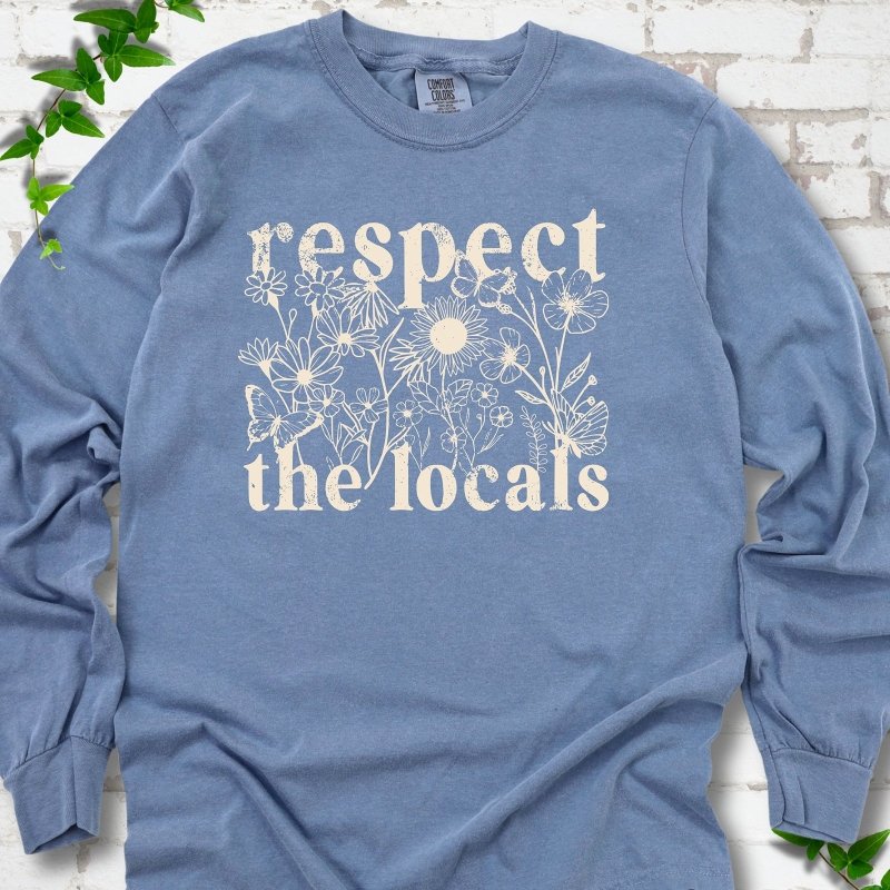 Blue Jean Comfort Colors® long sleeve T-shirt flat lay featuring the words Respect the Locals with native wildflowers and pollinators.