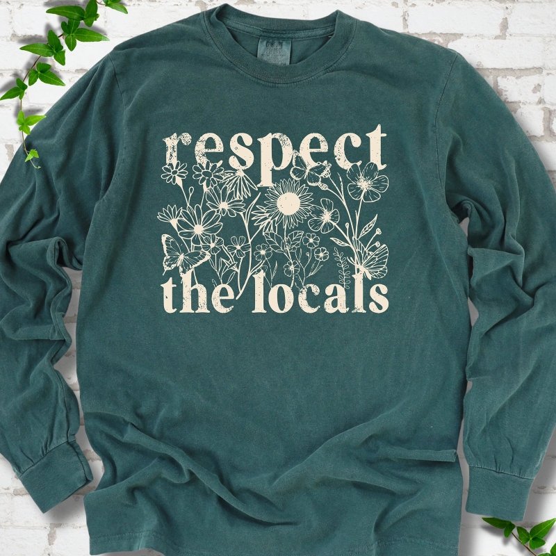 Blue Spruce Comfort Colors® long sleeve T-shirt flat lay featuring the words Respect the Locals with native wildflowers and pollinators.