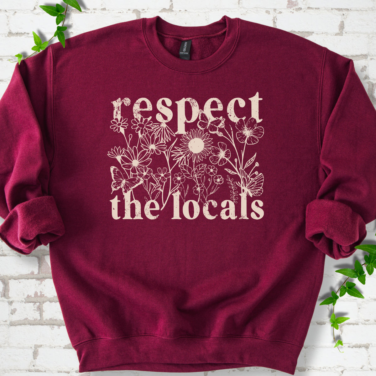 Maroon Gildan® 18000 crewneck sweatshirt flat lay featuring the words “Respect the Locals” with wildflowers and butterflies.