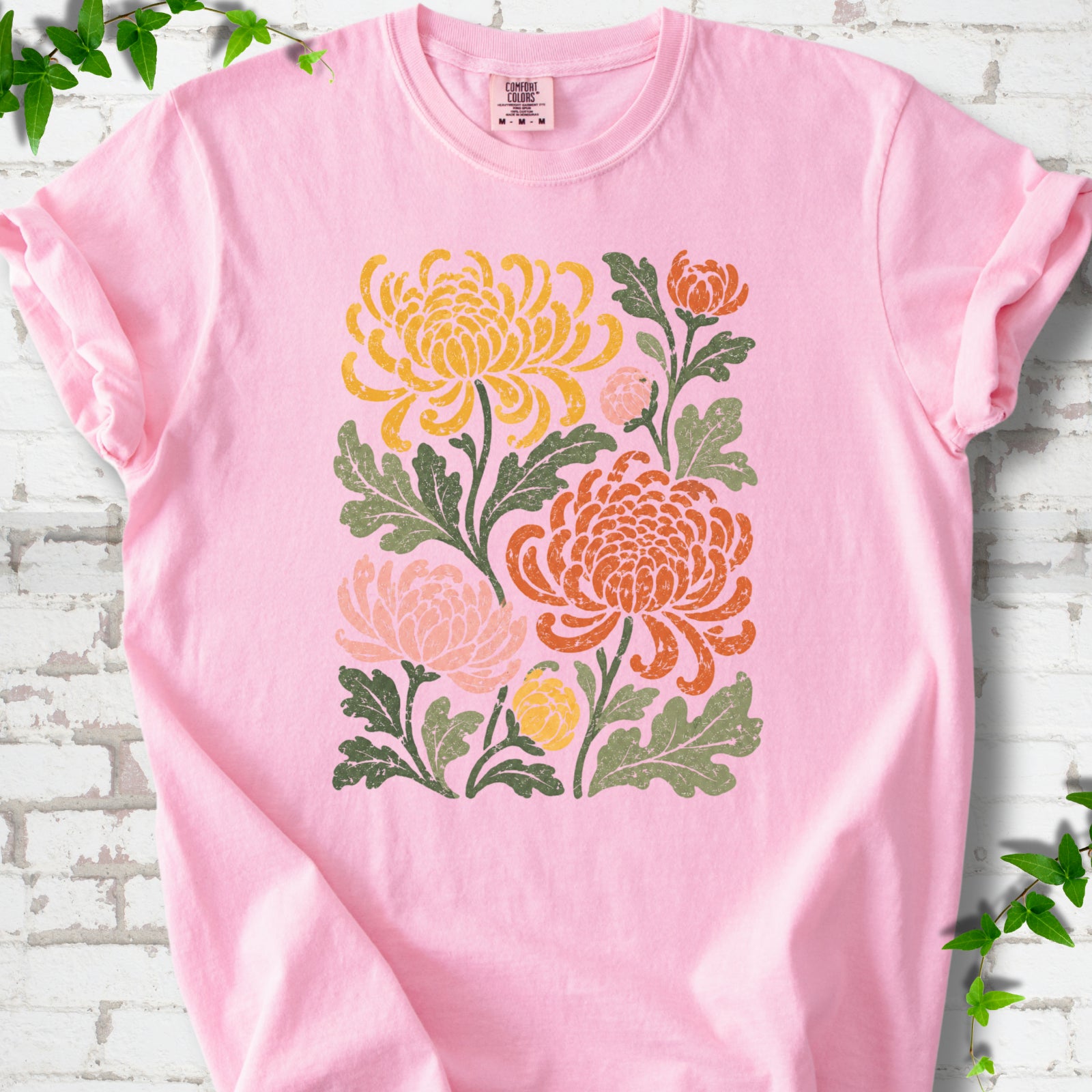 Blossom Comfort Colors® short sleeve T-shirt flat lay with a distressed multicolor chrysanthemum garden graphic on a white brick background with ivy accents