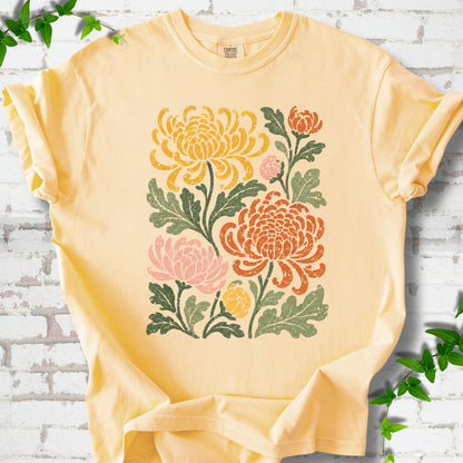 Butter Comfort Colors® short sleeve T-shirt flat lay with a distressed multicolor chrysanthemum garden graphic on a white brick background with ivy accents