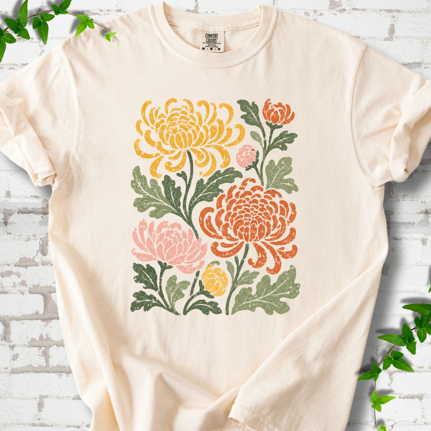 Ivory Comfort Colors® short sleeve T-shirt flat lay with a distressed multicolor chrysanthemum garden graphic on a white brick background with ivy accents