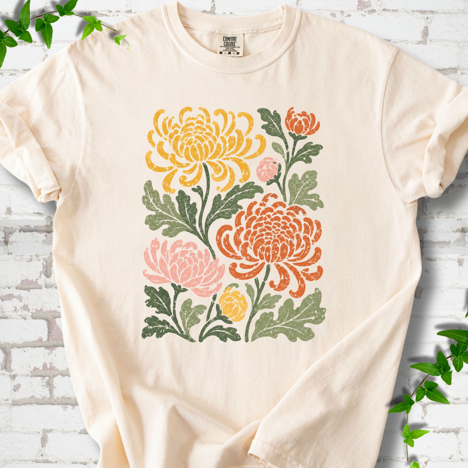 Ivory Comfort Colors® short sleeve T-shirt flat lay with a distressed multicolor chrysanthemum garden graphic on a white brick background with ivy accents