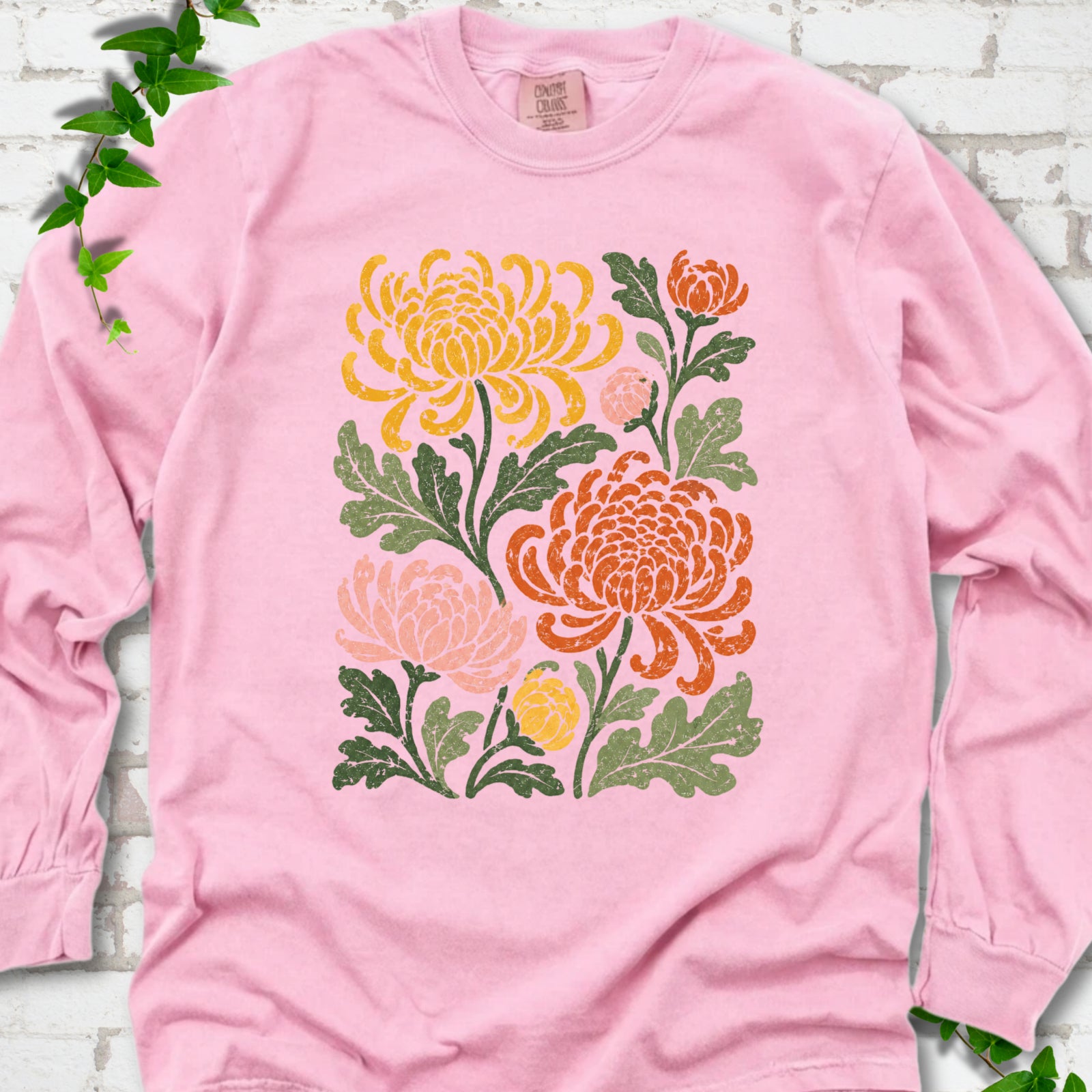 Blossom Comfort Colors® long sleeve T-shirt flat lay with a distressed multicolor chrysanthemum garden graphic on a white brick background with ivy accents