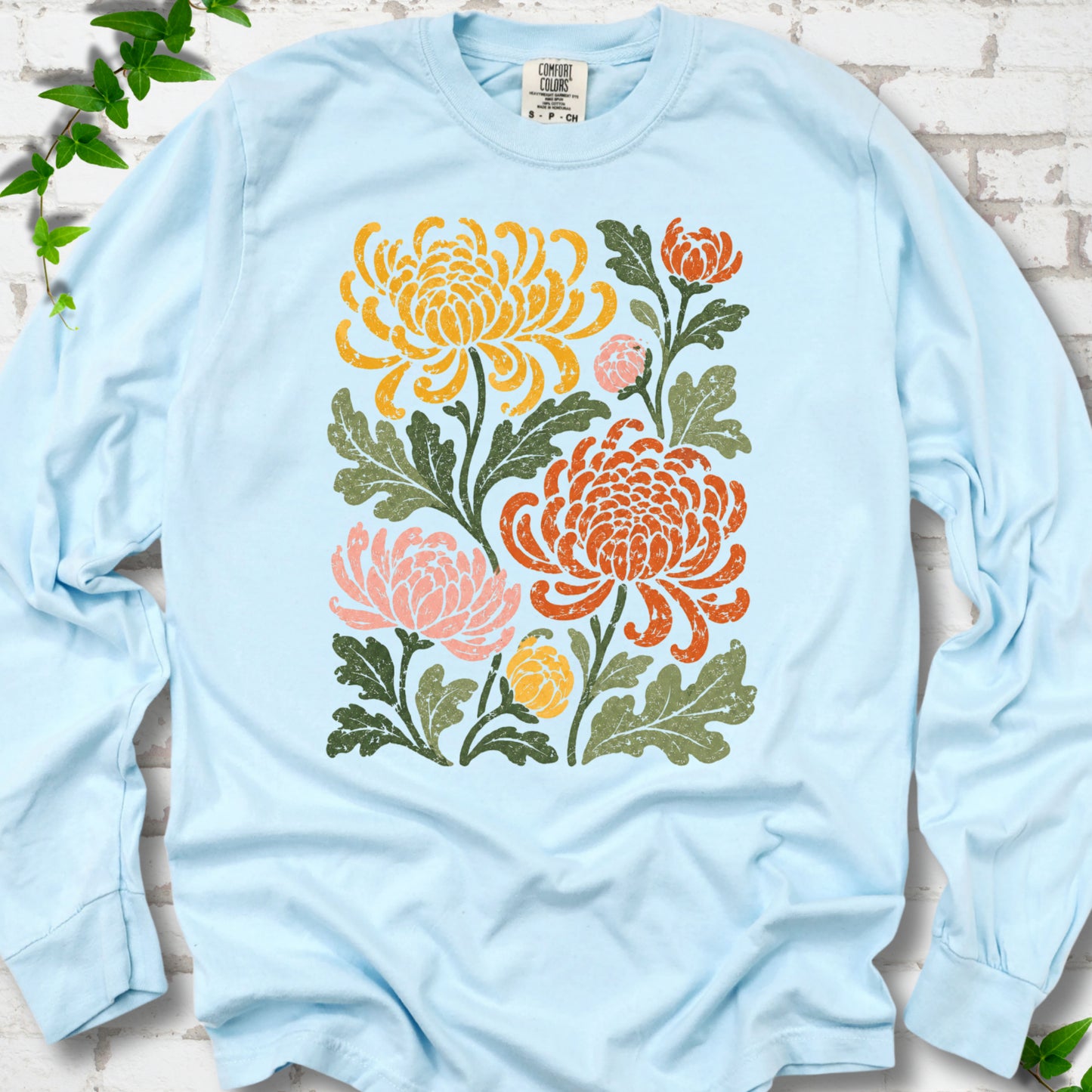 Chambray Comfort Colors® long sleeve T-shirt flat lay with a distressed multicolor chrysanthemum garden graphic on a white brick background with ivy accents