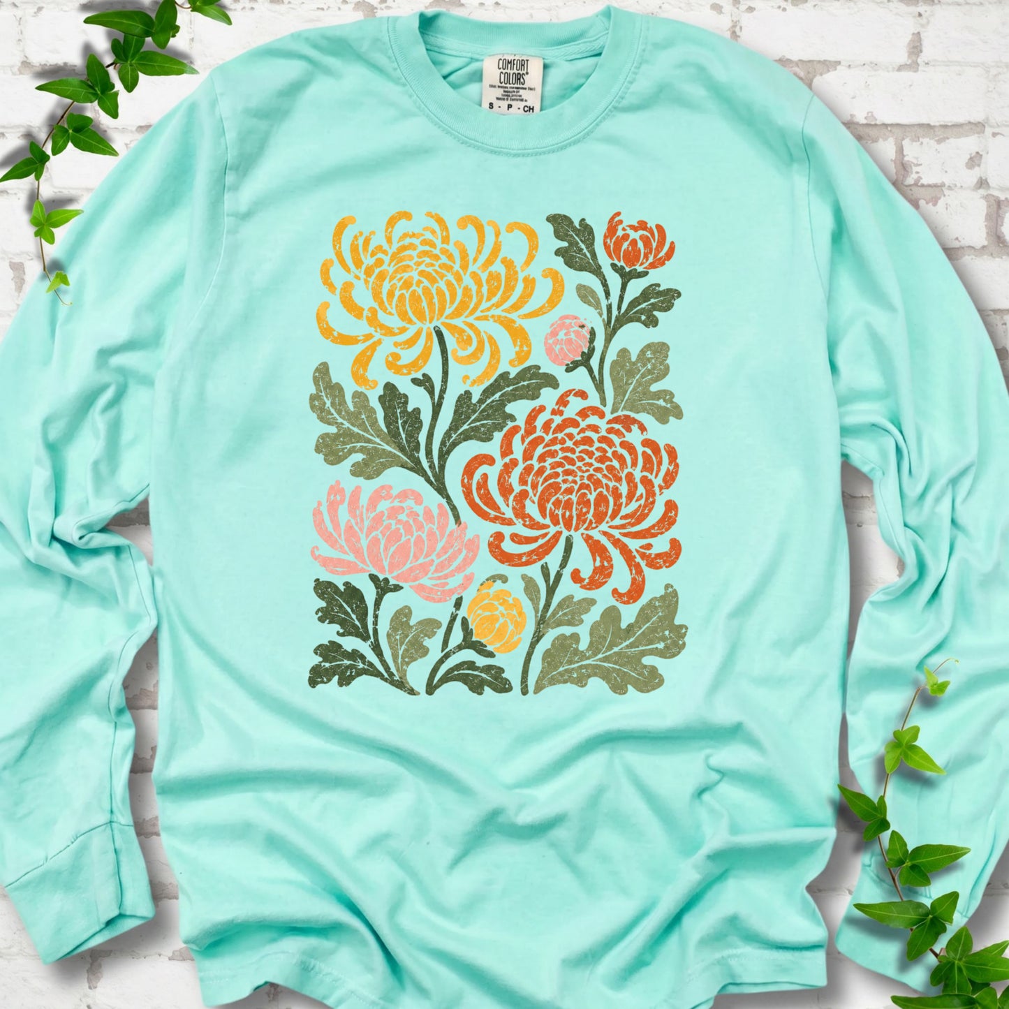 Island Reef Comfort Colors® long sleeve T-shirt flat lay with a distressed multicolor chrysanthemum garden graphic on a white brick background with ivy accents