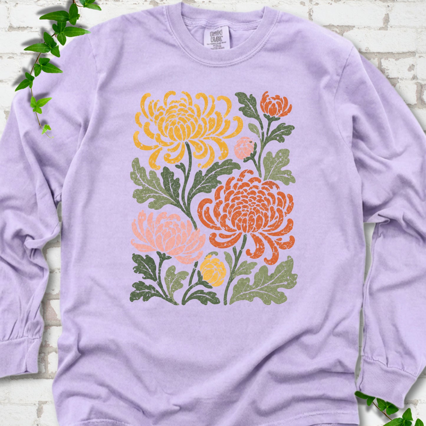 Orchid Comfort Colors® long sleeve T-shirt flat lay with a distressed multicolor chrysanthemum garden graphic on a white brick background with ivy accents