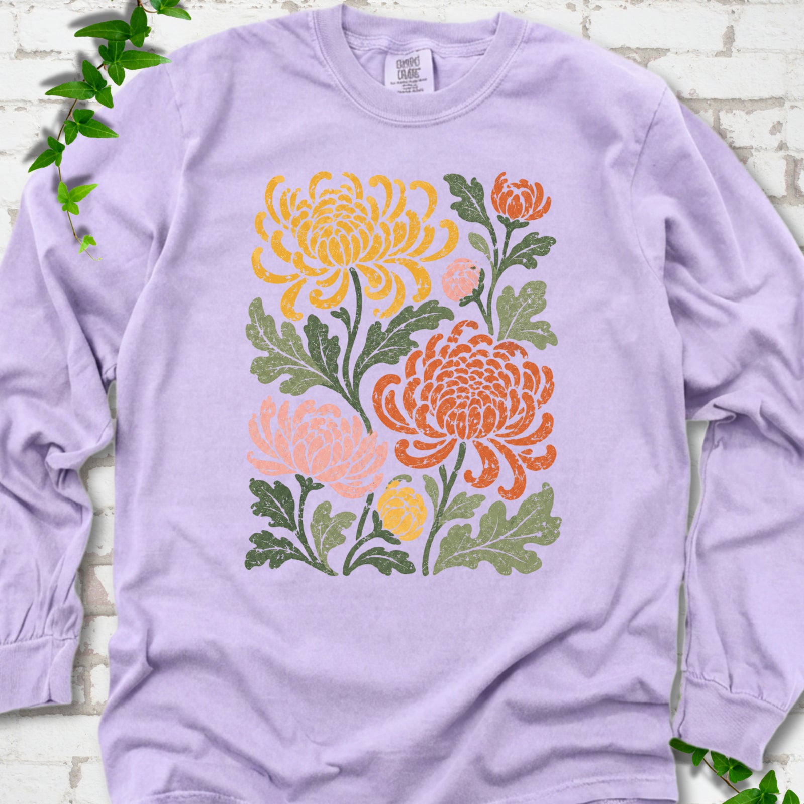 Orchid Comfort Colors® long sleeve T-shirt flat lay with a distressed multicolor chrysanthemum garden graphic on a white brick background with ivy accents
