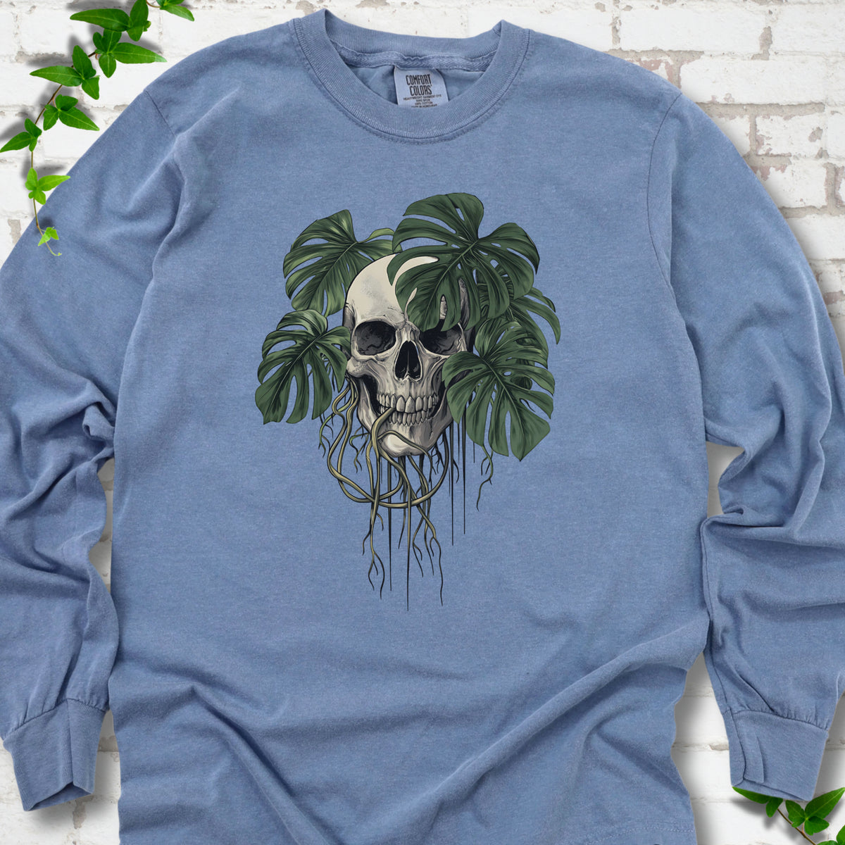 Blue Jean Comfort Colors T-shirt shown flat with the Root Bound Monstera skull and trailing roots graphic