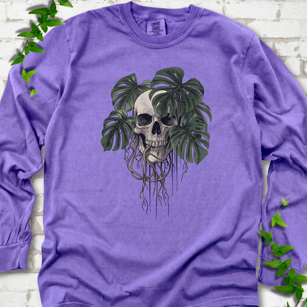 Violet Comfort Colors T-shirt shown flat with the Root Bound Monstera skull and trailing roots graphic
