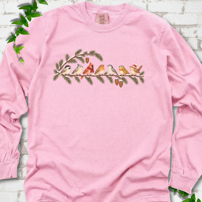Blossom long sleeve T-shirt laid flat, featuring seven songbirds on snowy evergreen branches with pinecones. Some birds wear scarves, and one wears a knit hat.