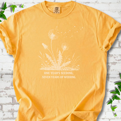 Citrus T-shirt flat lay with dandelion seed heads, drifting seeds and 'One year's seeding, seven years of weeding' lettering.