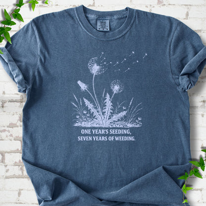 Denim T-shirt flat lay with dandelion seed heads, drifting seeds and 'One year's seeding, seven years of weeding' lettering.