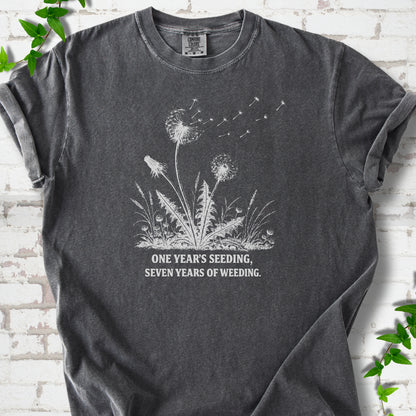 Pepper T-shirt flat lay with dandelion seed heads, drifting seeds and 'One year's seeding, seven years of weeding' lettering.