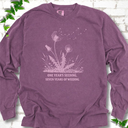 Berry long sleeve T-shirt flat lay with dandelion seed heads, drifting seeds and 'One year's seeding, seven years of weeding' lettering.