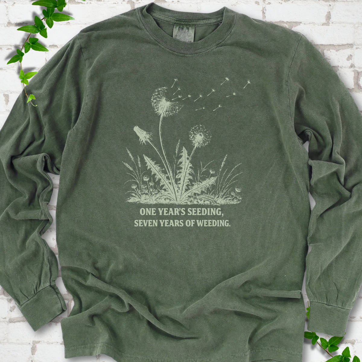 Hemp long sleeve T-shirt flat lay with dandelion seed heads, drifting seeds and 'One year's seeding, seven years of weeding' lettering.