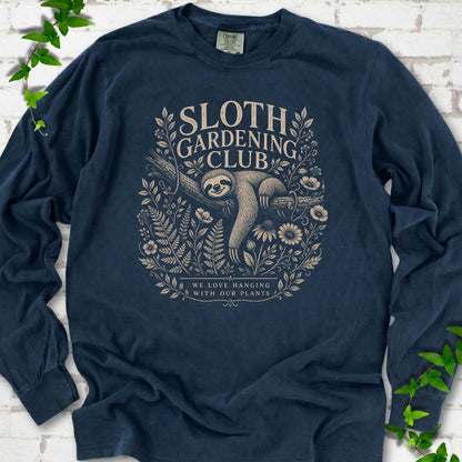 Midnight Comfort Colors® long sleeve T-shirt front mockup featuring a detailed cream-colored engraving-style illustration of a smiling sloth resting on a tree branch, surrounded by wild flowers and ferns.