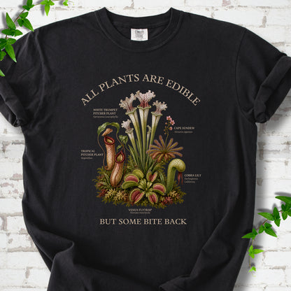 Black Comfort Colors® T-shirt front mockup featuring a botanical illustration of various carnivorous plants including a Venus Flytrap, Pitcher Plants, Cape Sundew, and Cobra Lily.