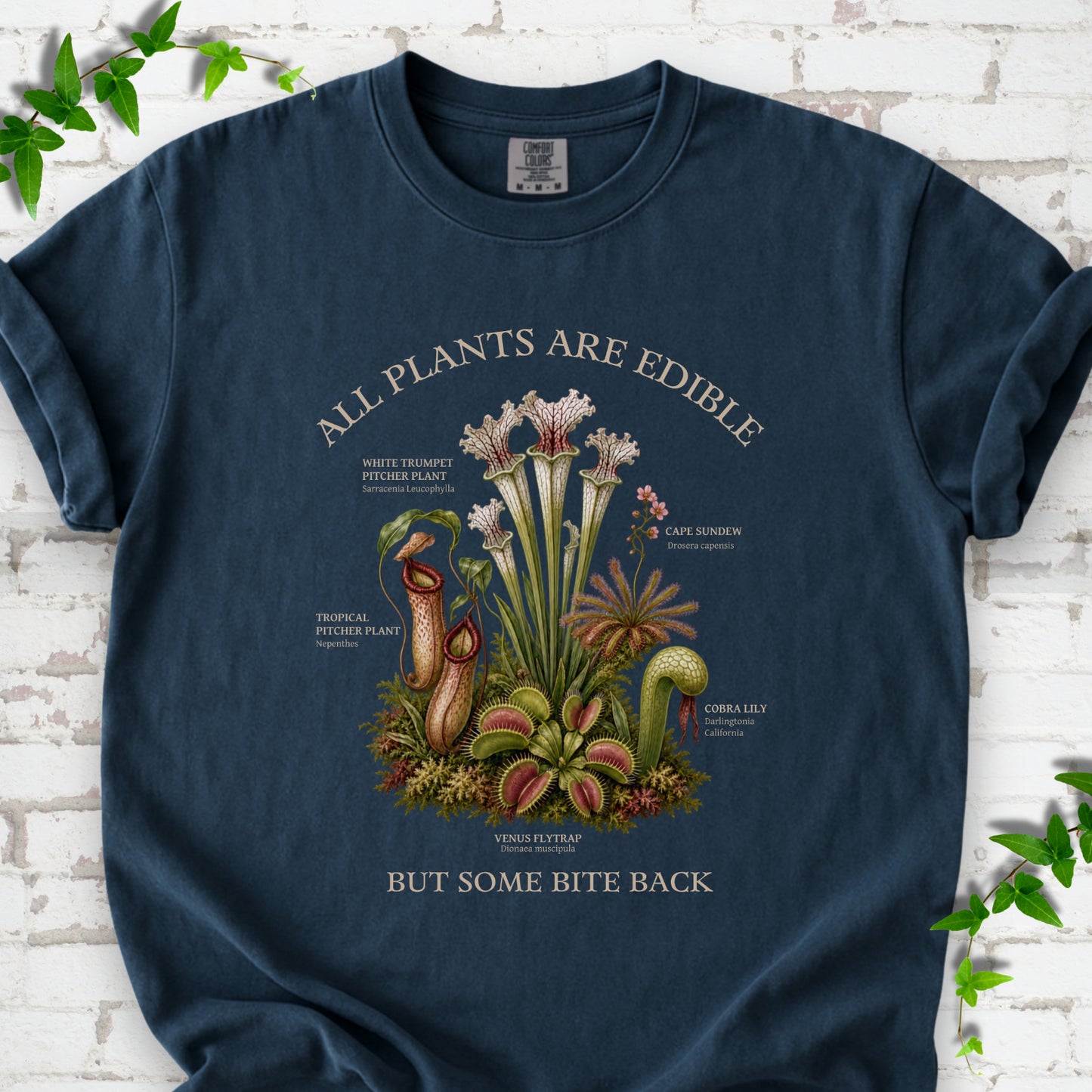 Midnight Comfort Colors® T-shirt front mockup featuring a botanical illustration of various carnivorous plants including a Venus Flytrap, Pitcher Plants, Cape Sundew, and Cobra Lily.