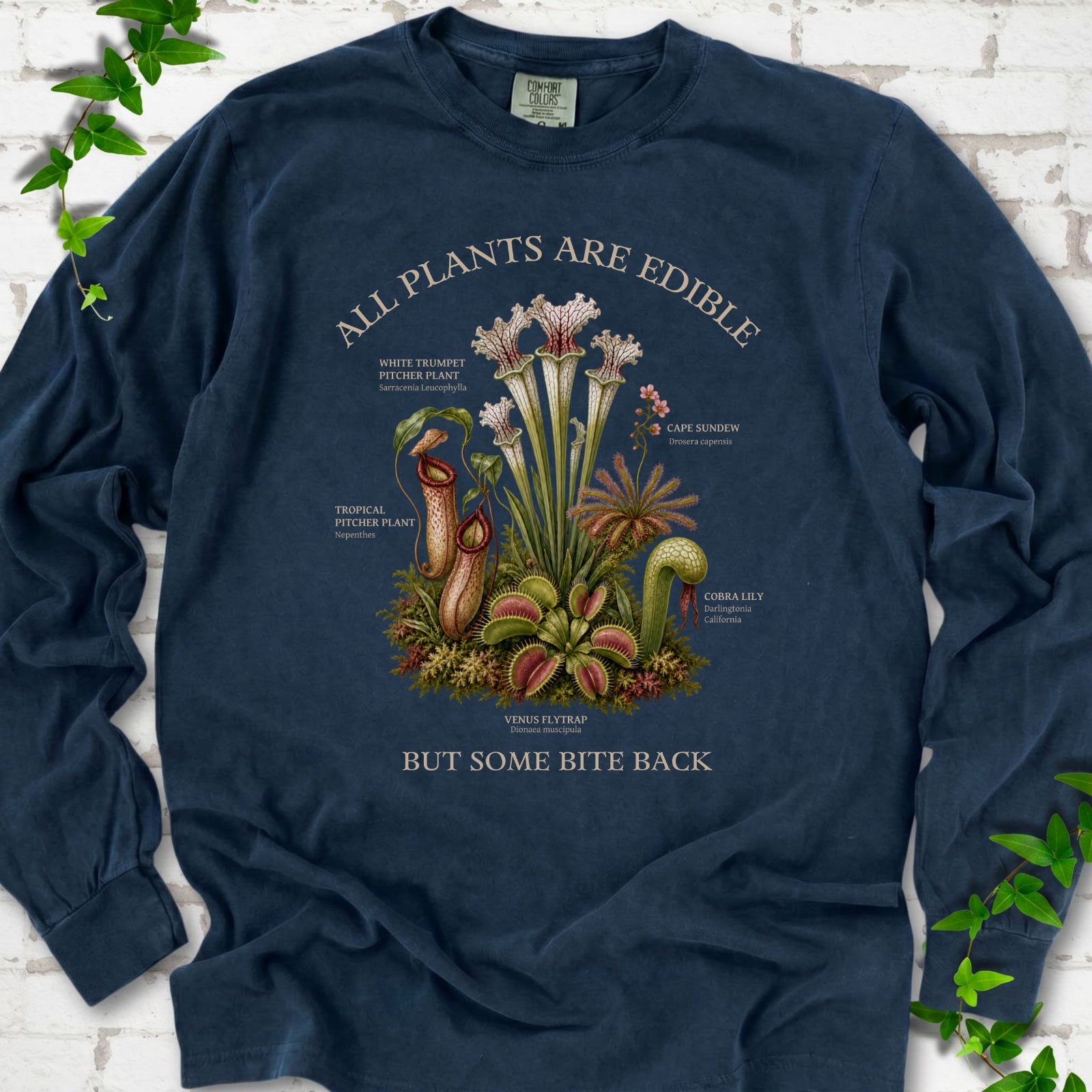 Midnight Comfort Colors® long sleeve T-shirt front mockup featuring a botanical illustration of various carnivorous plants including a Venus Flytrap, Pitcher Plants, Cape Sundew, and Cobra Lily.