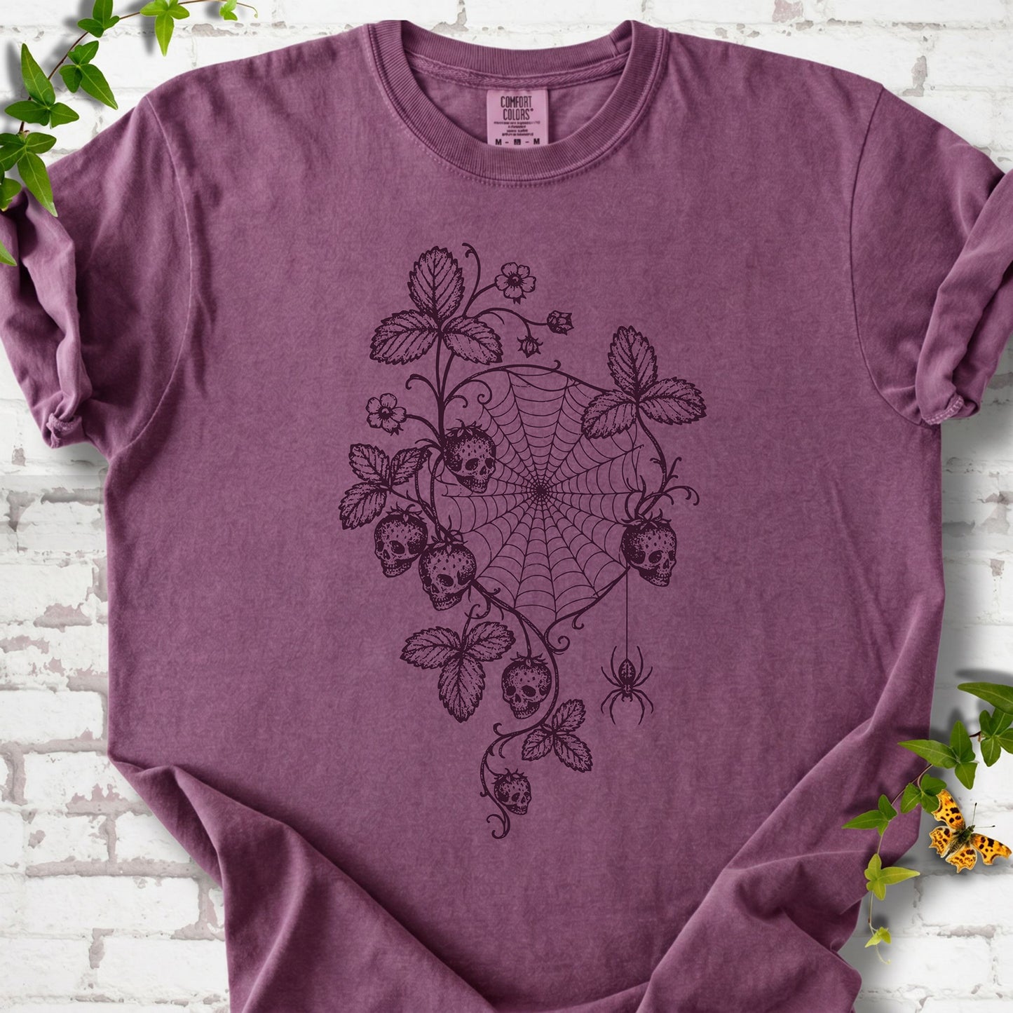 Berry Comfort Colors® T-shirt flat lay featuring skull-shaped strawberries, curling leaves, a spiderweb and a hanging spider.