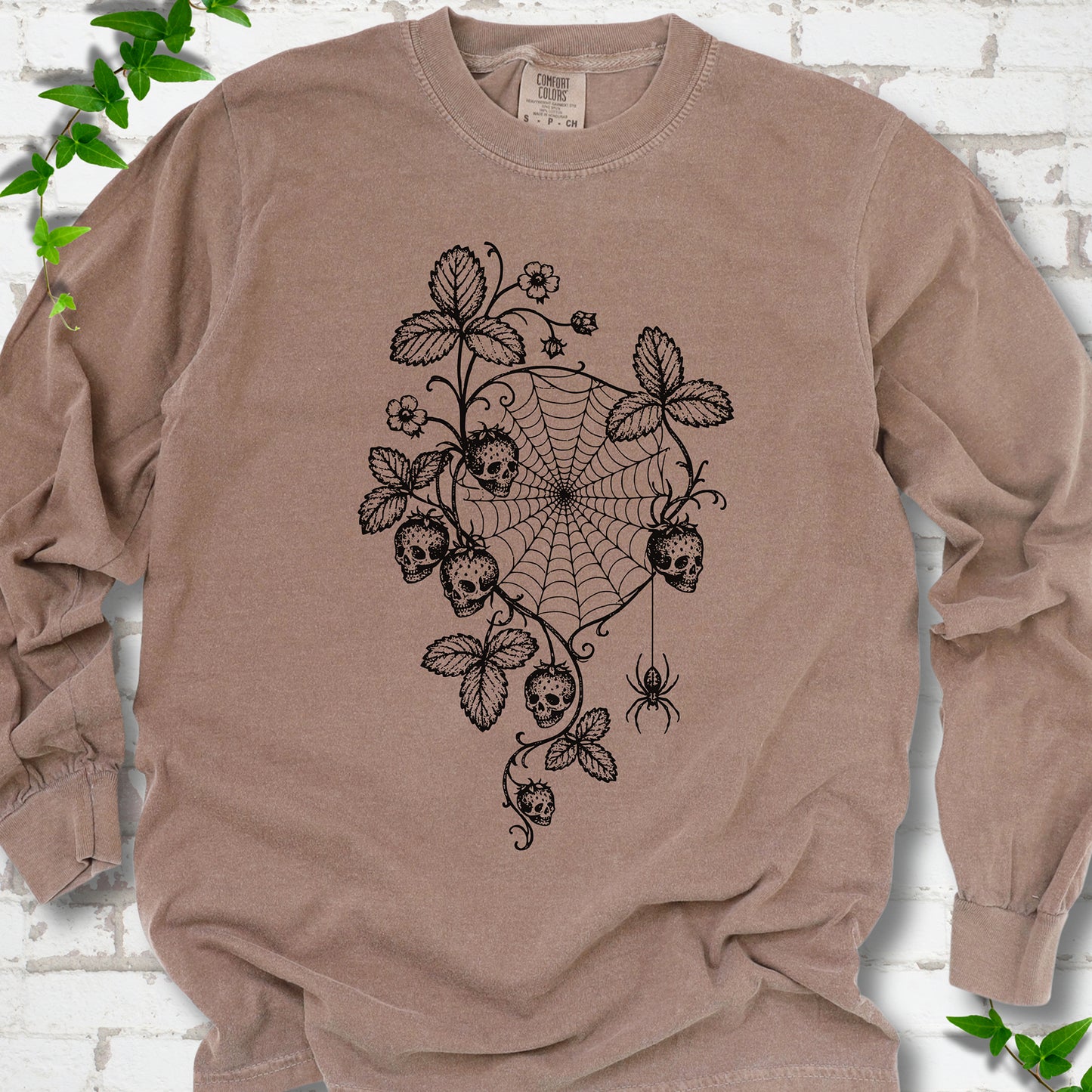 Espresso Comfort Colors® long sleeve T-shirt flat lay featuring skull-shaped strawberries, curling leaves, a spiderweb and a hanging spider.