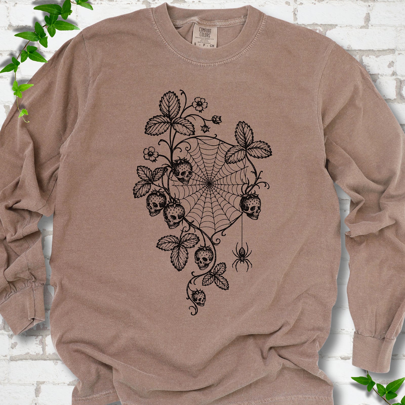 Espresso Comfort Colors® long sleeve T-shirt flat lay featuring skull-shaped strawberries, curling leaves, a spiderweb and a hanging spider.