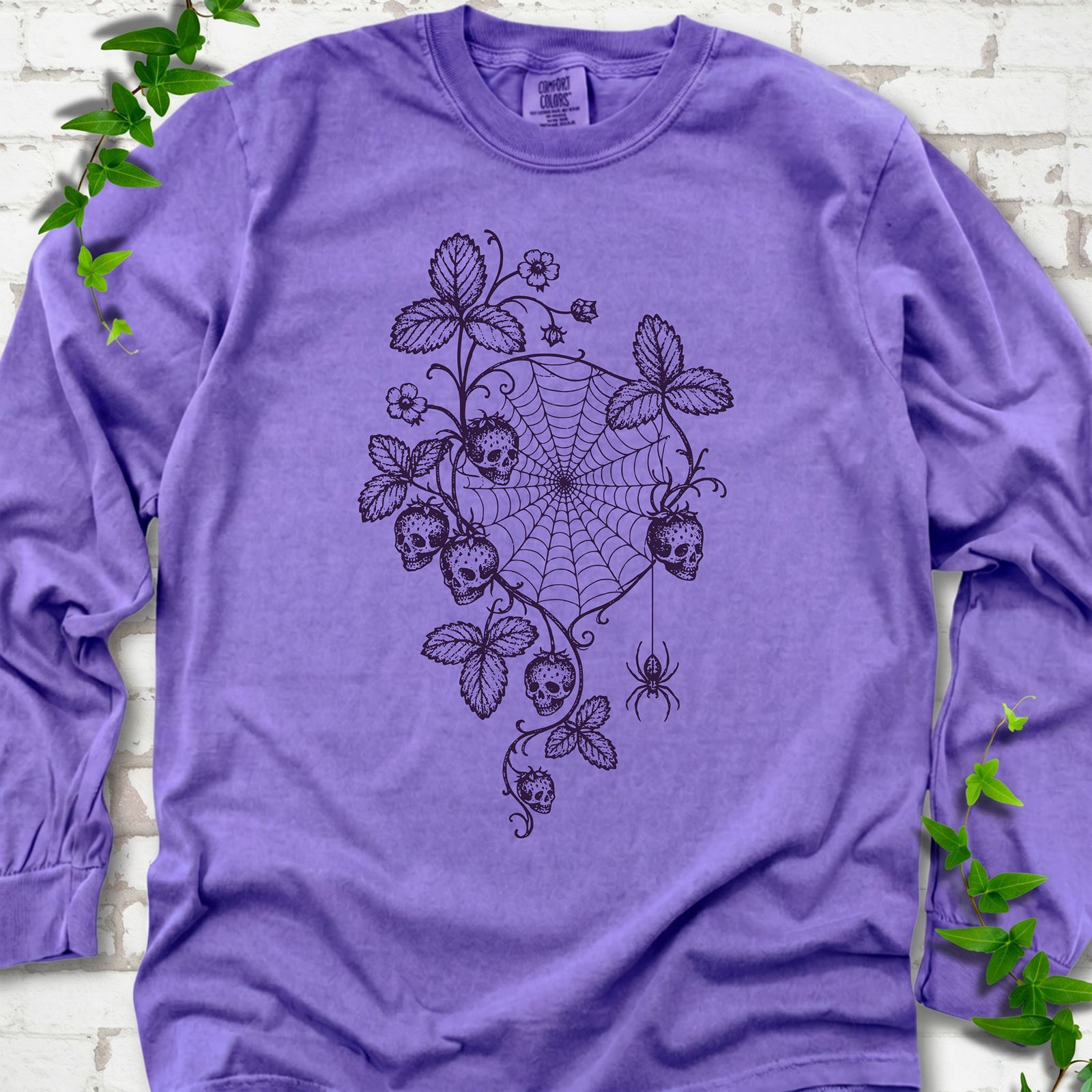 Violet Comfort Colors® long sleeve T-shirt flat lay featuring skull-shaped strawberries, curling leaves, a spiderweb and a hanging spider.
