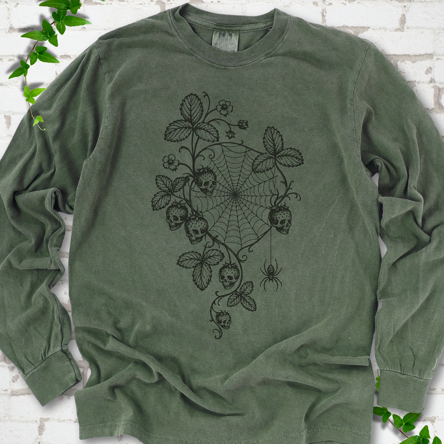 Hemp Comfort Colors® long sleeve T-shirt flat lay featuring skull-shaped strawberries, curling leaves, a spiderweb and a hanging spider.