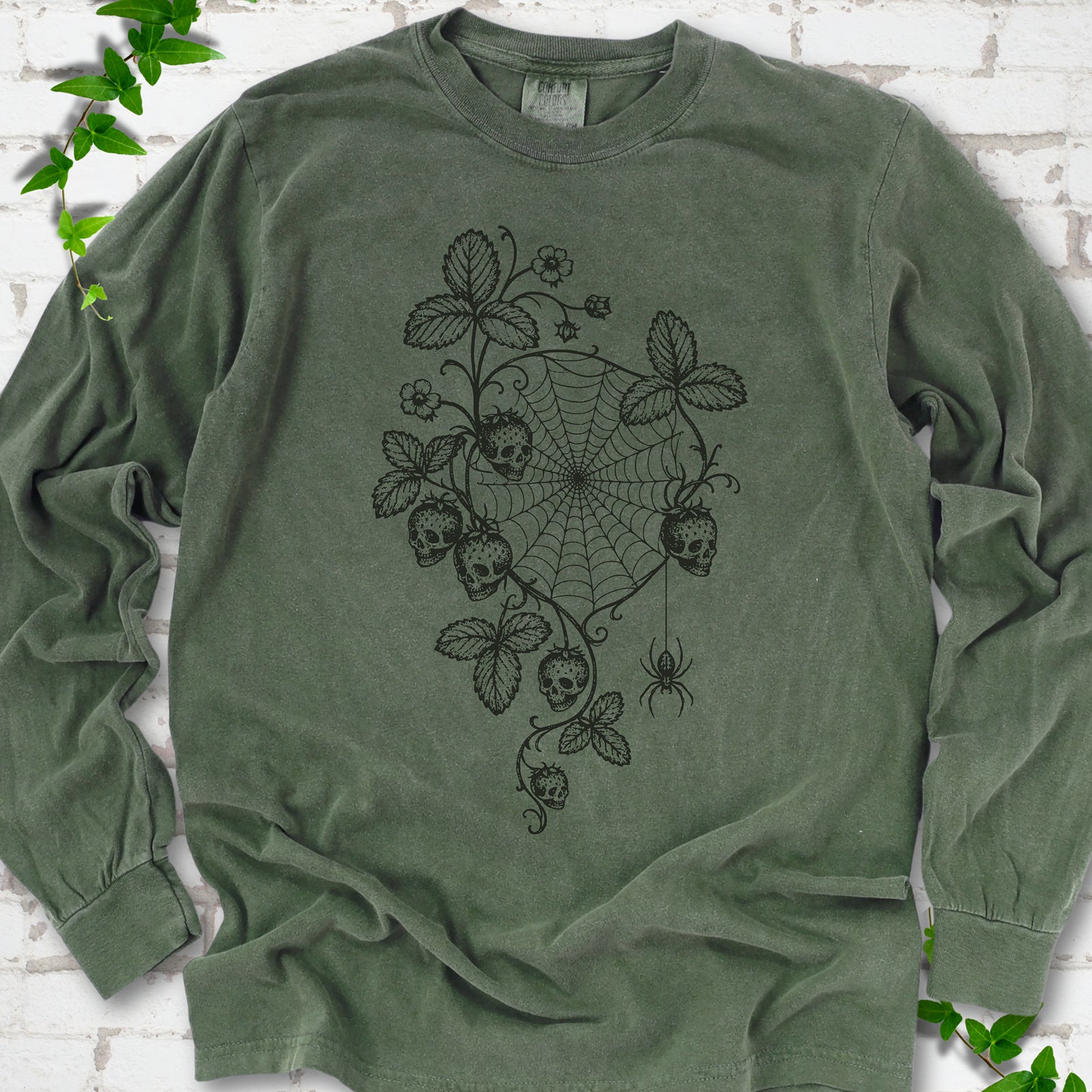 Hemp Comfort Colors® long sleeve T-shirt flat lay featuring skull-shaped strawberries, curling leaves, a spiderweb and a hanging spider.