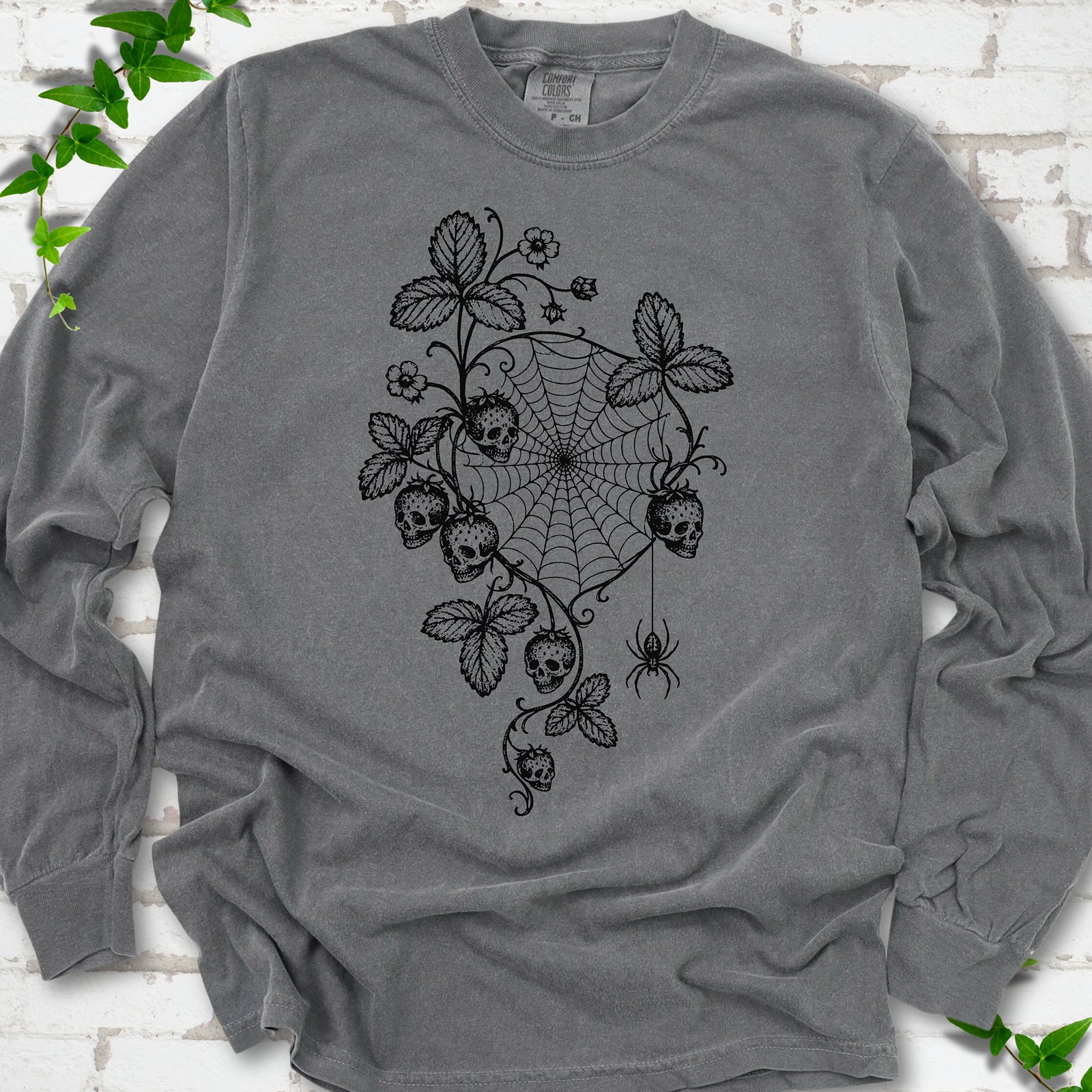 Pepper Comfort Colors® long sleeve T-shirt flat lay featuring skull-shaped strawberries, curling leaves, a spiderweb and a hanging spider.