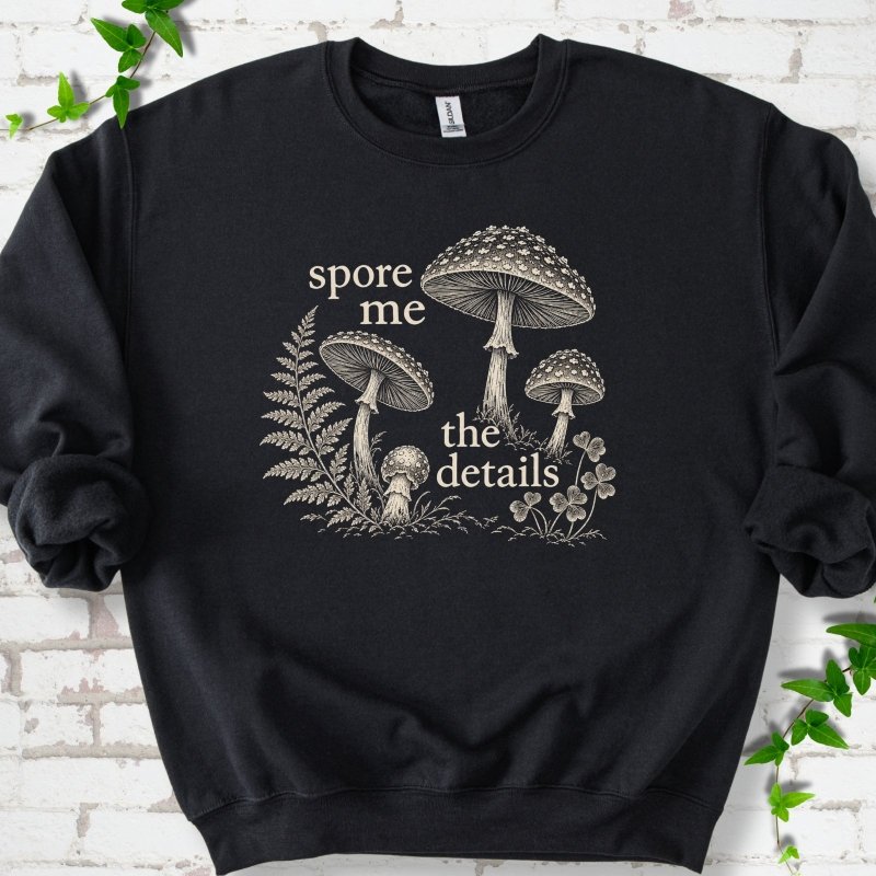 Black crewneck sweatshirt with "spore me the details" and engraved toadstools, fern and clover in cream ink
