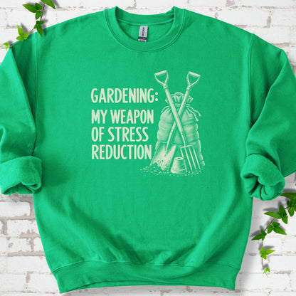 Irish Green sweatshirt flat lay with cream "Gardening: My Weapon of Stress Reduction" lettering beside a crossed spade and fork, burlap sack and a small flowerpot, edged by green leaves.