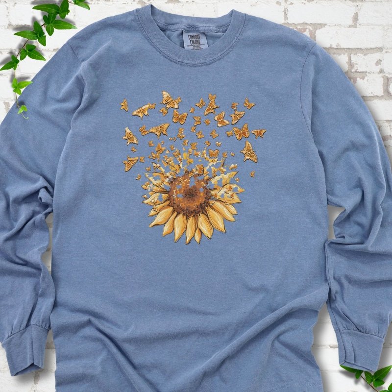 Blue Jean Comfort Colors® long sleeve T-shirt flat lay featuring a sunflower releasing a burst of orange butterflies.