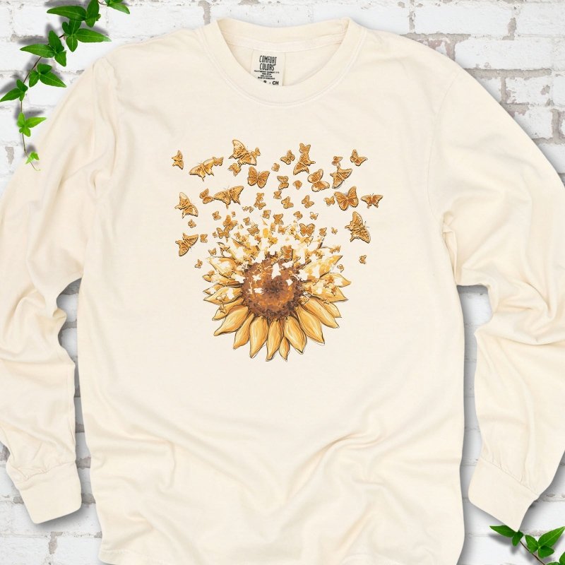 Ivory Comfort Colors® long sleeve T-shirt flat lay featuring a sunflower releasing a burst of orange butterflies.