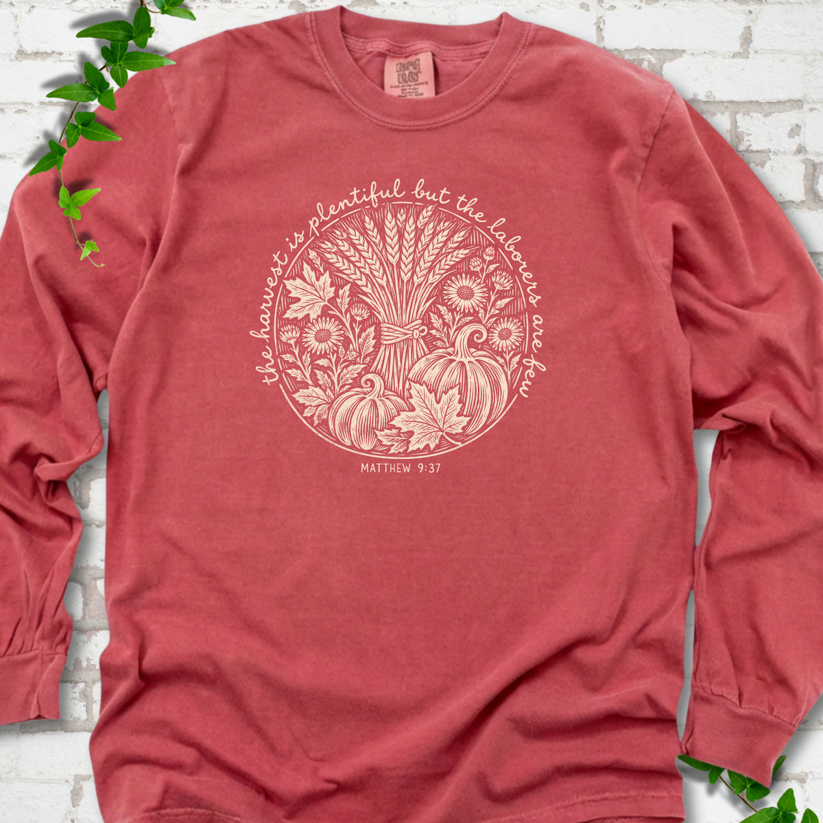 Crimson long sleeve T-shirt flat lay with cream wheat, pumpkins and leaves in a harvest circle, the Matthew 9:37 verse around it and its reference below.