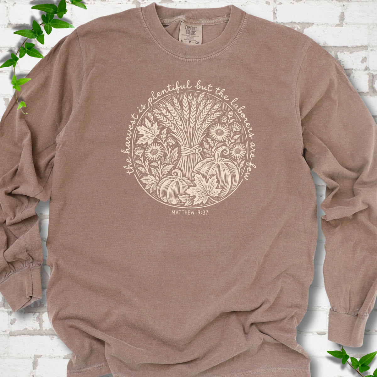 Espresso long sleeve T-shirt flat lay with cream wheat, pumpkins and leaves in a harvest circle, the Matthew 9:37 verse around it and its reference below.