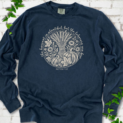 Midnight long sleeve T-shirt flat lay with cream wheat, pumpkins and leaves in a harvest circle, the Matthew 9:37 verse around it and its reference below.