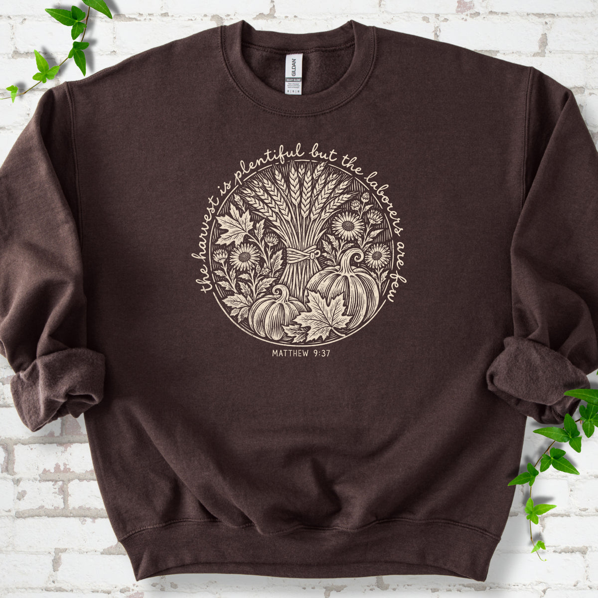 Dark Chocolate sweatshirt flat lay with cream wheat, pumpkins and leaves in a harvest circle, the Matthew 9:37 verse around it and its reference below.